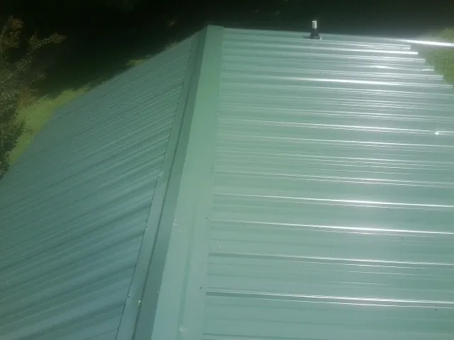 New green metal panels meeting at the ridge of a roof — Flat Roof Repair work by our crew in Everett