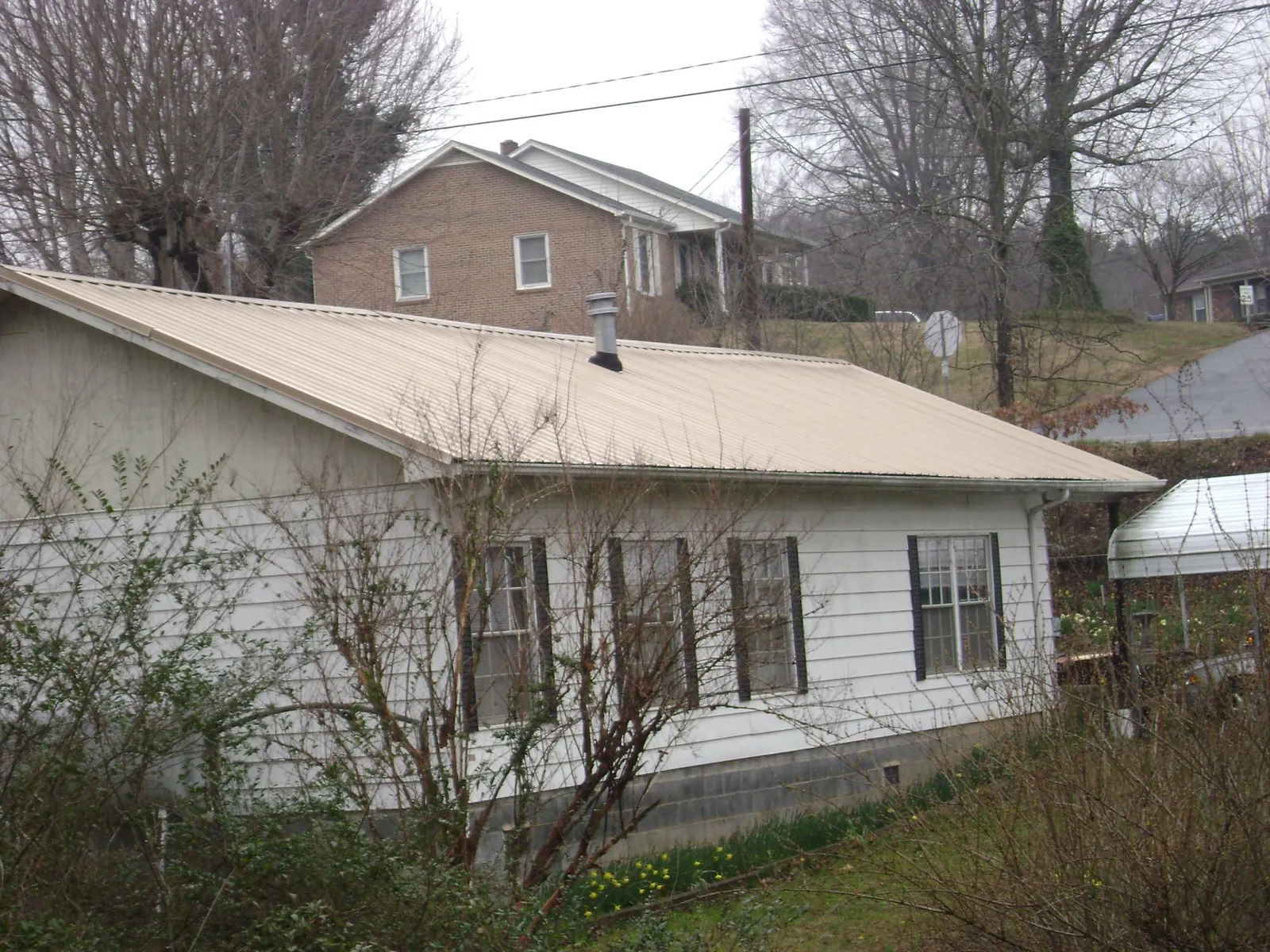 Tan metal roof on a white sided house set into a hillside — Commercial Roofing by Roofing Brothers in Everett